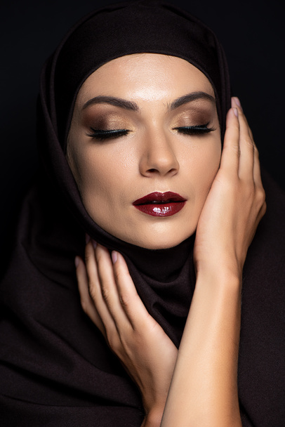 young Muslim woman in hijab with closed eyes, smoky eyes and red lips isolated on black - Fotografie, Obrázek