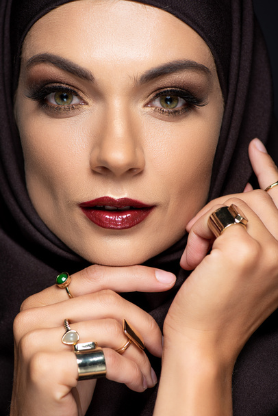 beautiful Muslim woman in hijab with makeup in golden rings isolated on black - 写真・画像