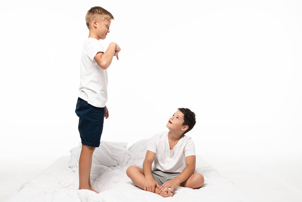 chlapec ukazuje prstem na bratra sedícího na posteli izolované na bílém - Fotografie, Obrázek