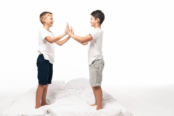 due fratelli sorridenti che battono le mani in piedi sul letto isolato su bianco
 - Foto, immagini