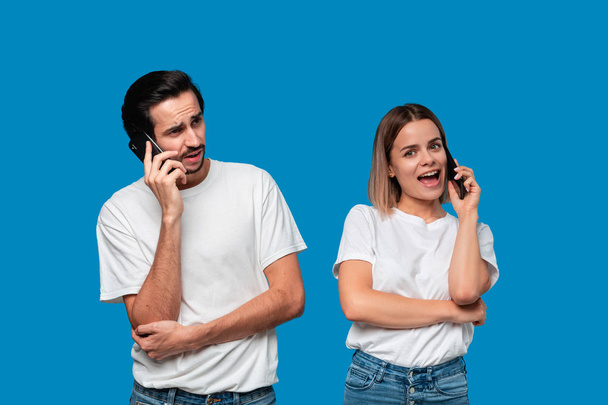 Blond woman and brunet man in white tees and blue jeans are talking on the phone. - Photo, Image