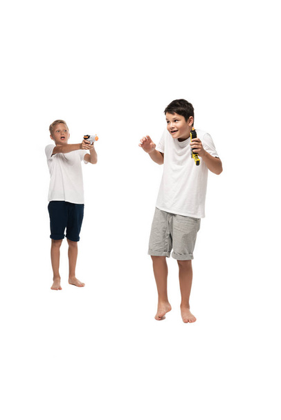 boy aiming with toy gun at scared brother on white background - Photo, Image