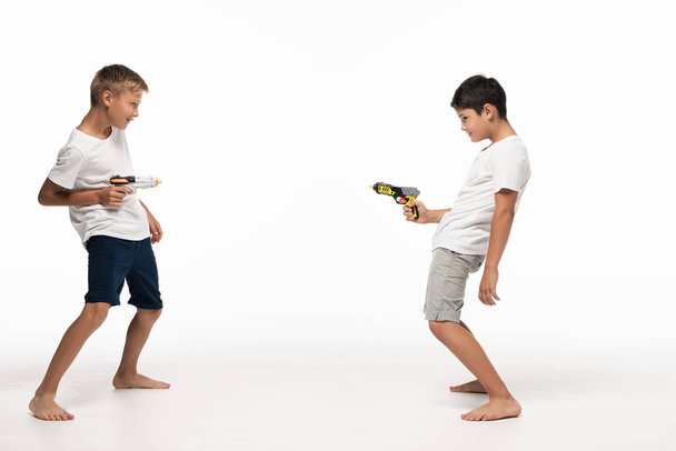 twee broers richten op elkaar met speelgoedgeweren op witte achtergrond - Foto, afbeelding