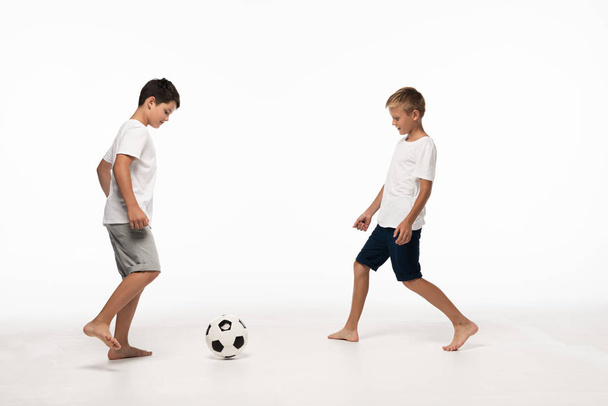 Δύο αδέρφια με πιτζάμες παίζουν ποδόσφαιρο σε λευκό φόντο - Φωτογραφία, εικόνα