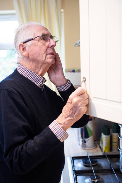 Forgetful Senior Man With Dementia Looking In Cupboard At Home - Foto, immagini