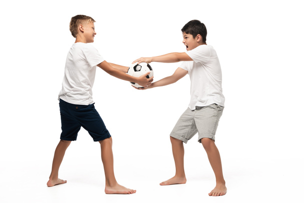 zlobivý chlapec brát fotbalový míč pryč od bratra na bílém pozadí - Fotografie, Obrázek