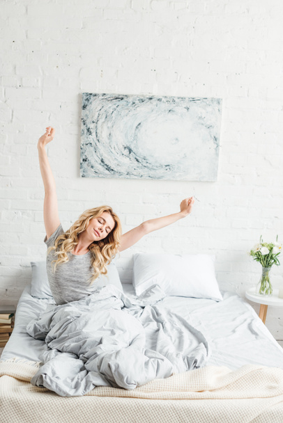 happy young woman sitting with outstretched hands while waking up at home  - Photo, Image
