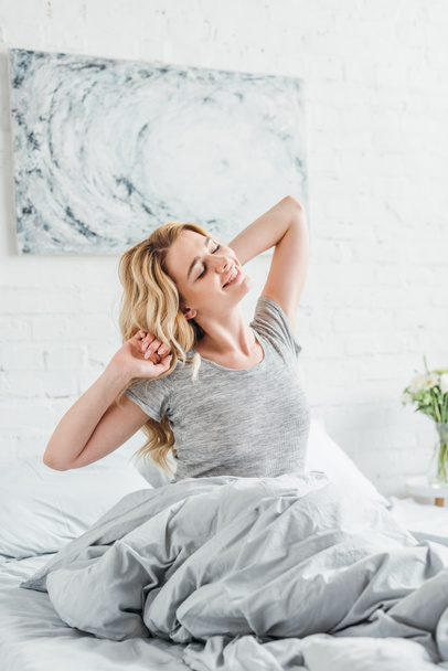 cheerful woman smiling while waking up in bedroom  - Photo, Image