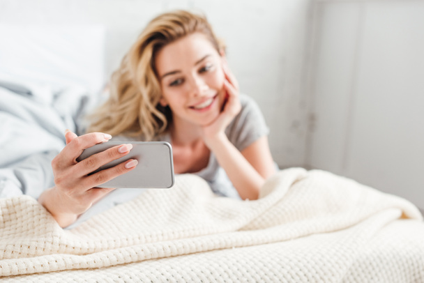 selective focus of happy girl taking selfie on smartphone while lying on bed  - 写真・画像
