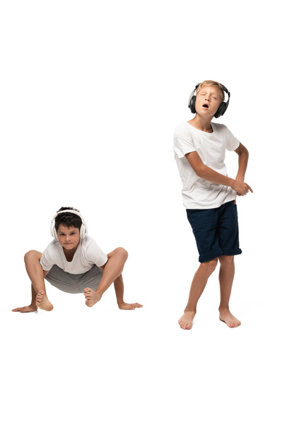 excited boy singing in headphones near brother sitting in frog pose on white background - Zdjęcie, obraz