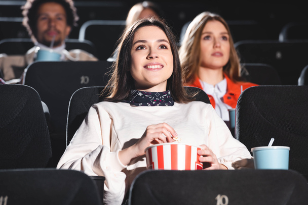 selective focus of smiling woman holding popcorn and watching movie in cinema - Fotoğraf, Görsel