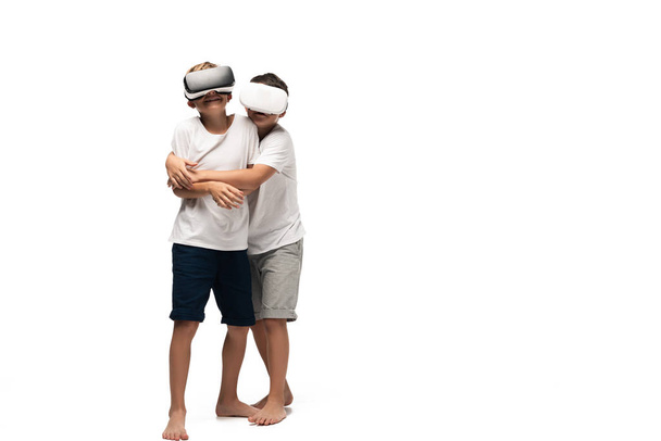 αγόρι αγκαλιάζει χαμογελαστός αδελφός, ενώ χρησιμοποιείτε ακουστικά VR μαζί σε λευκό φόντο - Φωτογραφία, εικόνα