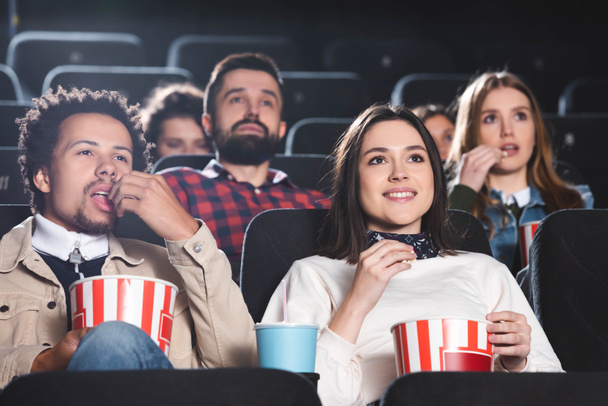 selective focus of multiethnic friends eating popcorn and watching movie in cinema  - Photo, Image
