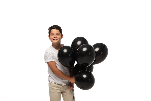 happy boy looking at camera while holding black balloons isolated on white - Foto, Imagem
