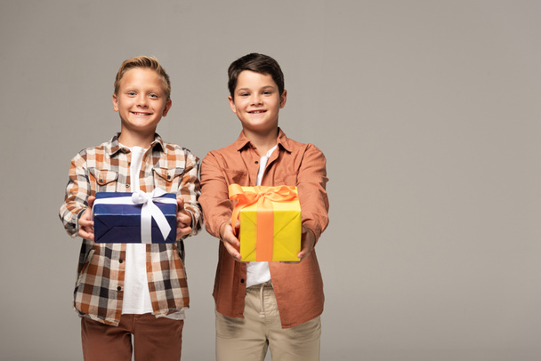 two happy brothers holding blue and yellow gift boxes isolated on grey - Foto, Imagen