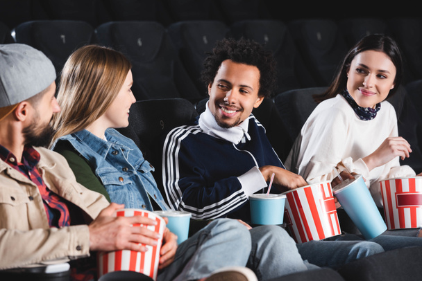 multikulturális barátok ülnek, mosolyognak és beszélgetnek a moziban  - Fotó, kép