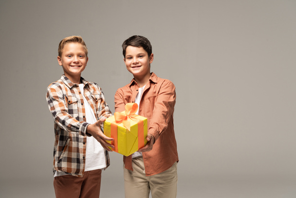 kaksi onnellista veljeä näyttää keltaista lahjapakkausta eristettynä harmaaseen
 - Valokuva, kuva