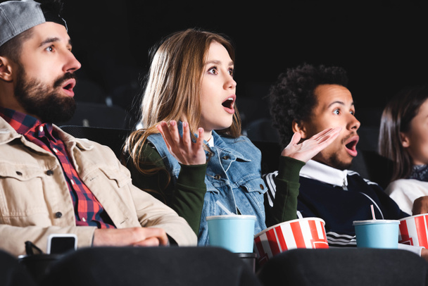 shocked multicultural friends with popcorn watching movie in cinema  - Photo, Image