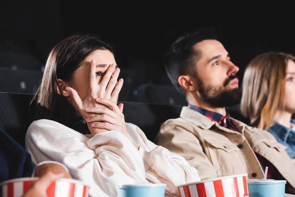 恐怖の女性が顔を隠して映画館で友人と映画を見ているという選択的焦点  - 写真・画像