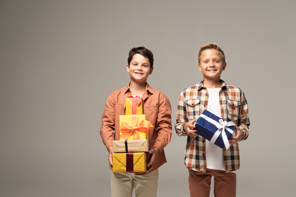 deux frères heureux tenant des boîtes-cadeaux multicolores et souriant à la caméra isolée sur gris
 - Photo, image