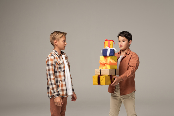 surprised boy holding stack of multicolored gift boxes near amazed brother isolated on grey - Fotoğraf, Görsel