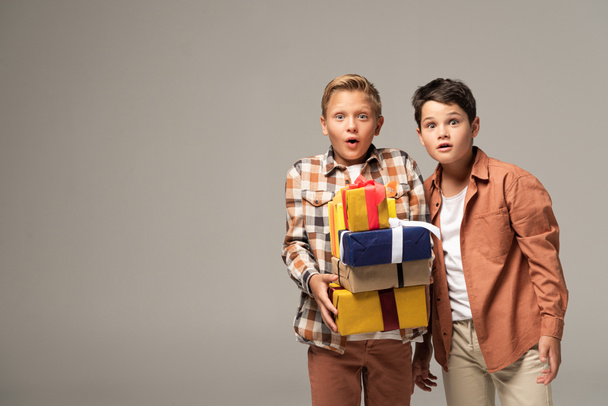 two surprised brothers showing stack of gift boxes isolated on grey - Foto, imagen