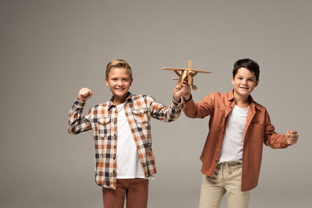 dos hermanos alegres sosteniendo avión de juguete, mostrando sí gesto y mirando a la cámara aislada en gris
 - Foto, Imagen