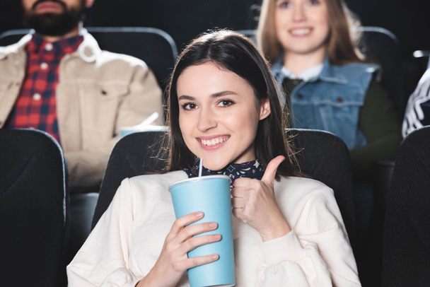 Selektive Fokussierung einer lächelnden Frau, die im Kino Sympathie zeigt und Pappbecher hält  - Foto, Bild