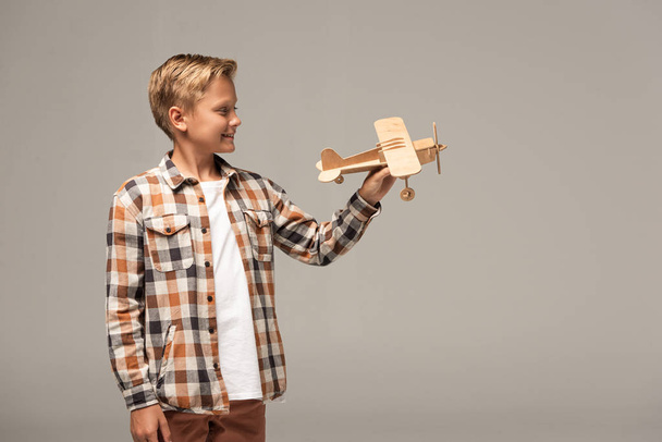 smiling boy holding wooden toy plane isolated on grey - Photo, Image