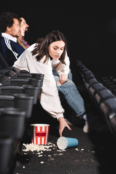 atrakcyjna kobieta biorąc papierowy kubek z sodą z podłogi w kinie  - Zdjęcie, obraz