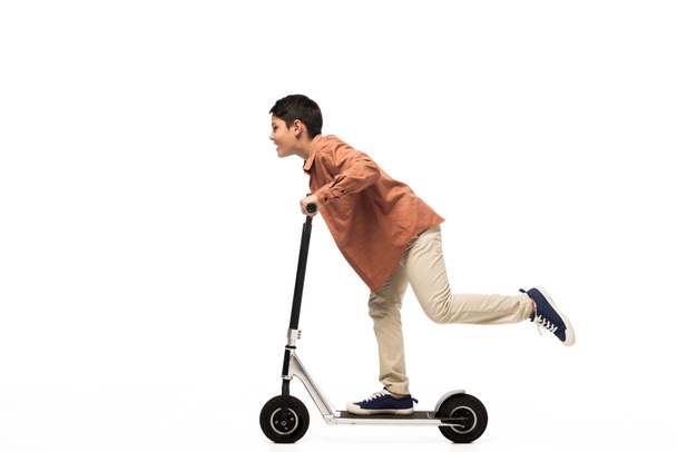 side view of smiling boy riding kick scooter on white background - Photo, Image