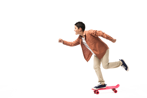 side view of cheerful boy riding kick scooter on white background - Photo, Image