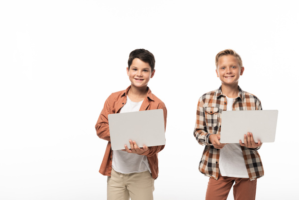 Два улыбающихся брата, держащих ноутбуки и улыбающихся в камеру, изолированные на белом
 - Фото, изображение