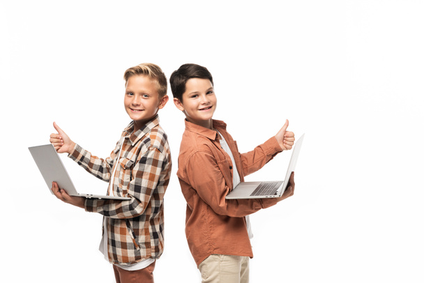 Два улыбающихся брата держат ноутбуки, показывают большие пальцы вверх и смотрят на камеру, изолированную на белом
 - Фото, изображение