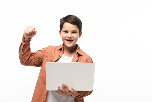 veselý chlapec drží notebook a ukazuje vítězný gesto izolované na bílém - Fotografie, Obrázek