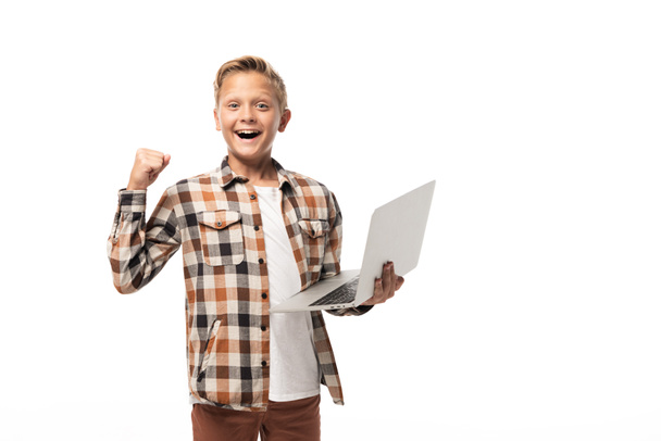 fröhlicher Junge hält Laptop in der Hand, zeigt Siegergeste und blickt isoliert auf weiße Kamera - Foto, Bild