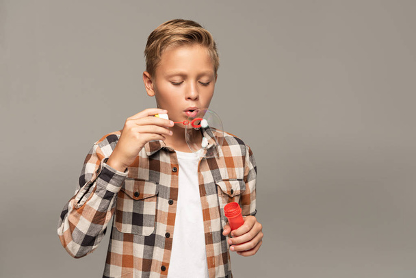 cute boy blowing soap bubbles isolated on grey - 写真・画像