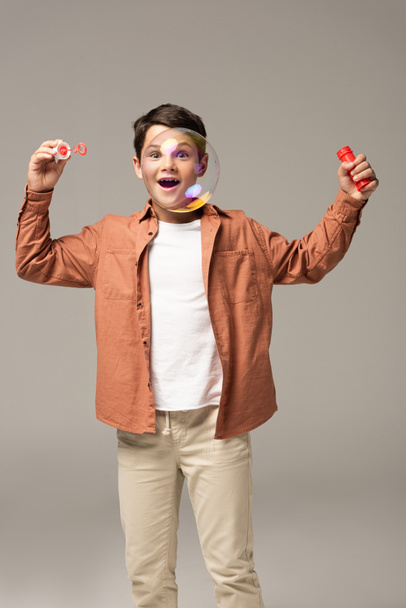 menino espantado olhando para bolha de sabão isolado em cinza
 - Foto, Imagem