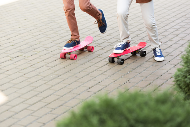 cropped view of two boys riding penny boards on pavement - Foto, imagen