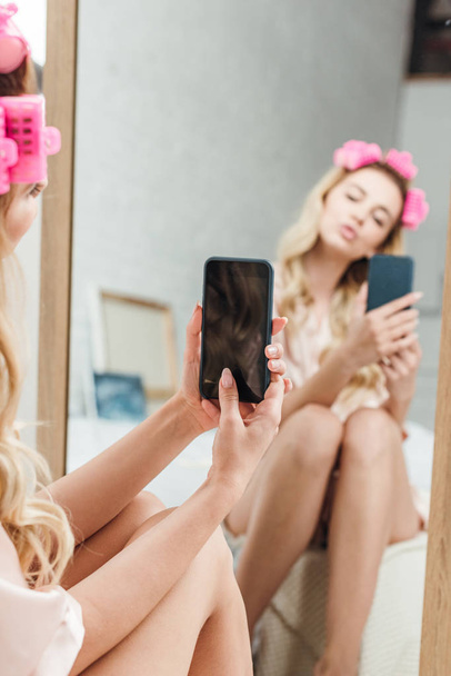 selectieve focus van de vrouw met eendengezicht houden smartphone terwijl het nemen van foto in de buurt van spiegel  - Foto, afbeelding