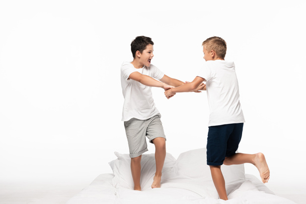 dwóch braci walczących dla zabawy biały stojąc na łóżku odizolowany na białym - Zdjęcie, obraz