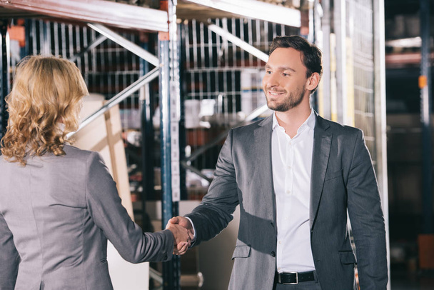 glimlachende zakenman schudden handen met zakenvrouw in magazijn - Foto, afbeelding