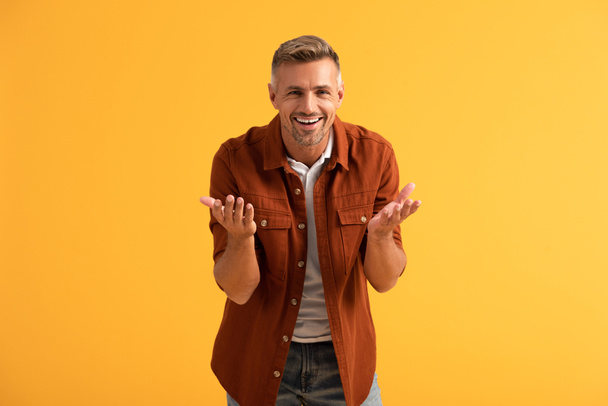 happy man looking at camera and gesturing isolated on orange  - Foto, afbeelding