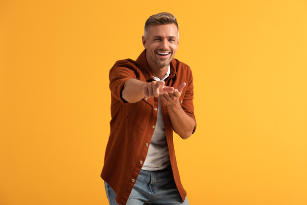 selectieve focus van blije man kijkend naar camera en wijzend met vinger geïsoleerd op oranje  - Foto, afbeelding