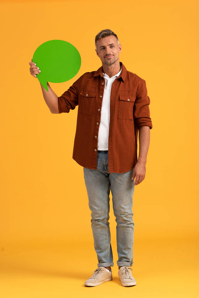 happy man holding green speech bubble on orange  - Foto, afbeelding