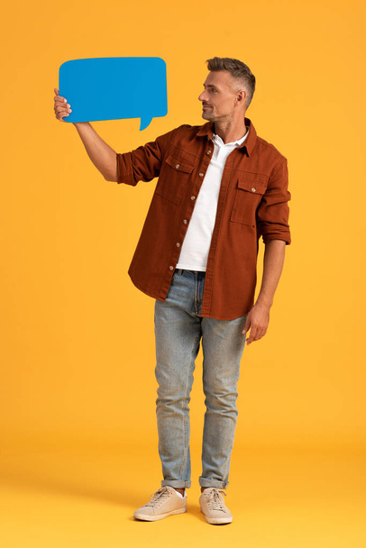 handsome man holding blue speech bubble and standing on orange  - Фото, изображение