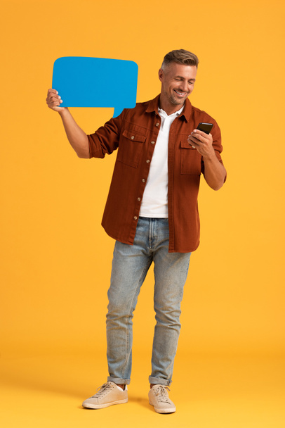 šťastný muž drží modré řeči bublina a smartphone na oranžové  - Fotografie, Obrázek