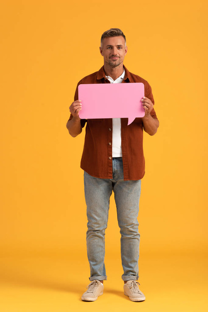happy man holding pink speech bubble and standing on orange  - 写真・画像