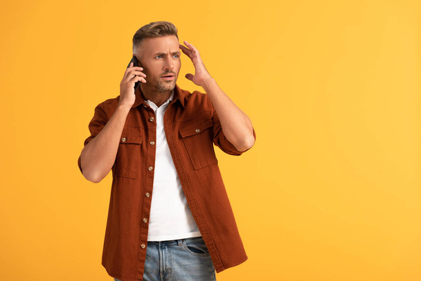 Emotionaler Mann gestikuliert beim Telefonieren auf Smartphone isoliert auf Orange  - Foto, Bild