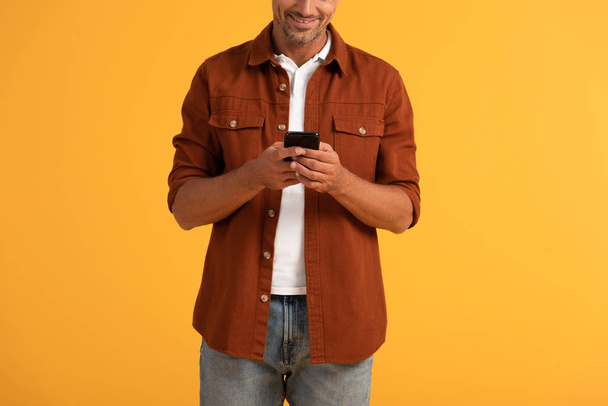 vista recortada de hombre feliz usando teléfono inteligente aislado en naranja
  - Foto, imagen